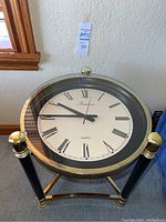 Full view of the brass clock table showing its oval quartz clock face and brass and black legs.