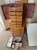 Jewelry chest with side panels open showing hanging necklaces and top drawers open with jewelry compartments; trays on floor