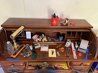 Wide view of desk rolltop with multiple office items including brass worklight, pens, rulers, paperweight, scissors, tape dispensers and stapler.