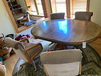 Wide shot of oval wooden pedestal game table with four upholstered armchairs arranged around it.