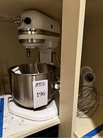 White KitchenAid Heavy Duty bowl-lift stand mixer with stainless steel mixing bowl and wire whisk attachment beside it.