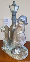 Full view of the Lladro figurine showing girl with rake, lamp post, fence, and dog.