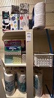 Photo showing boxes of Kleenex tissues with different prints, pack of Quilted Northern toilet paper, paper towel rolls, and a white plastic storage bin.