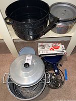 Overview photo showing black speckled canning pots, pressure cooker, a fondue pot burner stand, and blue Tupperware containers inside a shelf space.