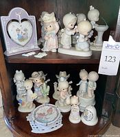 Collection of Precious Moments figurines, decorative plates, and frames arranged on wooden shelves.