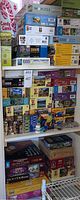 Shelf with stacked assorted puzzle boxes of various brands with scenes such as moons, flowers, buildings, and abstract patterns, mostly 500 to 1000 piece puzzles.