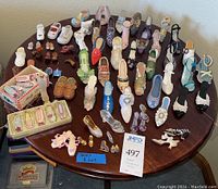 Full overview of laid out miniature shoe collection on round wooden table, showing shoes in multiple colors, sizes, and styles with a focus on the full set and shoe perfume bottle.
