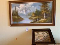 Both paintings hung on a wall showing the large mountain and lake scene above the smaller deer landscape painting.