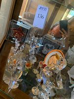 Multiple clear and colored Swarovski crystal figurines including birds, flowers, and pineapple shown on glass shelf.