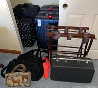 Five luggage pieces: three large black check-in suitcases with spinner wheels, two black carry-on style bags (one with quilted texture), two wooden suitcase holders with red and green striped straps, a bright orange luggage strap, and a small horse-themed bag on wheels.
