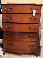 Front view of vintage wooden dresser with five drawers and ornate metal handles.