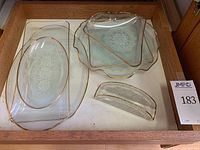 Seven vintage glass plates and a dish with lace designs and gold rims arranged in a drawer.
