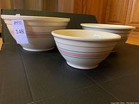 Three vintage McCoy nesting mixing bowls shown next to each other, displaying cream color with blue and pink stripes.