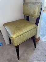 Side view of vintage sewing chair with gold embossed vinyl upholstery and wood turned legs.