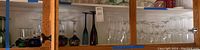 Shelf with multiple rows of clear wine glasses, colored glasses including blue, green and amber cut crystal goblets, and other stemware.