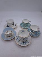 Overview of all 5 cups and saucers with different floral designs and gold trims.