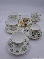 Full view of all six cups and their matching saucers with floral patterns and gold rim accents on white porcelain.