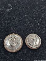 Photo of two antique French compacts on a black background, showing embossed floral and female profile lids.