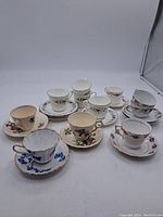 Photo showing all nine cups and saucers arranged with various floral patterns and gold trim detailing.