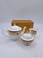 Set of three pieces including teapot, creamer, and sugar bowl with original box in background.