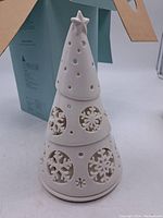 Front view of ceramic tealight holder shaped like a Christmas tree with star top and multiple snowflake cutouts.