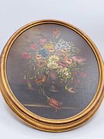Overall front view of circular framed oil painting showing floral bouquet in vase with gold frame