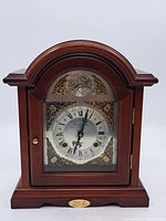 Front view of wooden mantel clock with glass door, arched top, and brass knob