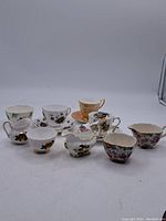 Eight assorted vintage fine bone china teacups with floral decorations, displayed upright.