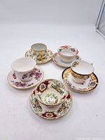 Five fine bone china teacups and saucers arranged together, showing different floral patterns and gold detailing.