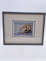 Framed watercolor artwork showing full view of otter in water and frame.