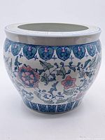 Front view showing the floral and leaf pattern decoration on the jar body with blue geometric designs at the base, on a white glazed porcelain surface.