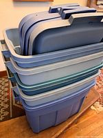 Stacked large Rubbermaid storage totes in various shades, with lids resting inside the top tote