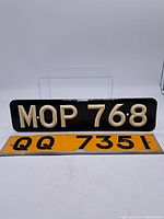 Photo showing two number plates: one black with white characters 'MOP 768' and one yellow with black characters 'QQ 7351'.