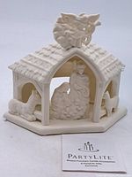 Porcelain nativity stable with textured roof and angel on top, flank by sheep figures