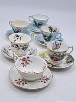 Overall view of six bone china teacups with matching saucers, displayed in two rows showing distinct hand-painted floral patterns and gold trim on each piece.