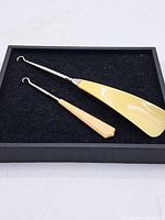 Both antique buttonhooks displayed side by side on black felt inside a black frame. Shows full length and handle detail.