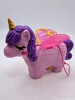 Side view of vintage Polly Pocket pink winged horse figurine with purple mane and yellow horn, showing the design details and handle on top.