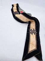 Full view of the Masonic sash showing black velvet edges with a central beige fabric strip and attached metal cross emblems.