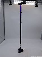 Purple adjustable walking stick with black foam handle, quad rubber base, and wrist strap in studio setting.