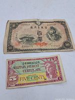 Photo shows both Japanese 100 yen bill and US Military Payment Certificate 5 cents note laid flat.