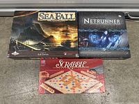 Boxed SeaFall, Android Netrunner, and Scrabble board games in a set.