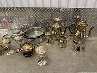 Photo of brass and silver-plated teapots, iridescent sugar bowl, silver goblets and small creamer or sugar bowl
