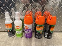 Five OFF! brand bug spray bottles, two white pump spray bottles, one purple aerosol can, two black aerosol cans with orange caps, on a metal background.