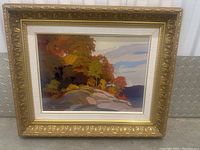 Full view of framed painting showing autumnal trees, rocky shore and lake