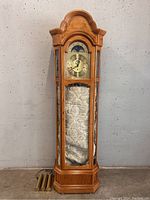 Full view of the grandfather clock showing oak wood case, brass dial with moon phase, and glass panels.