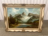 Full view of oil painting showing mountainous landscape with lake and trees, framed in ornate decorative frame.