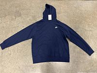 Full view of the navy blue Nike hoodie sweater laid flat on a concrete floor showing front side with hood, long sleeves, and front pocket.