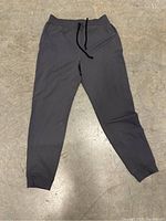 Front view of a single pair of large grey sweatpants laid flat on a concrete floor showing waistband, drawstring, and cuffed ankles.