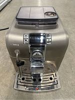 Front view of stainless steel espresso machine showing control panel, bean hopper lid, and drip tray
