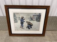 Full front view of the framed artwork showing children playing in the snow with a house and snowy trees in the background.